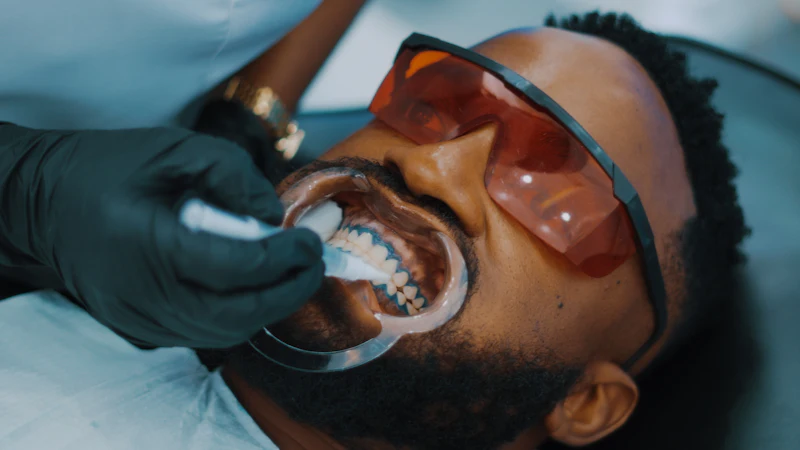 A dentist cleaning a patient's teeth with a small brush while the patient wears protective glasses