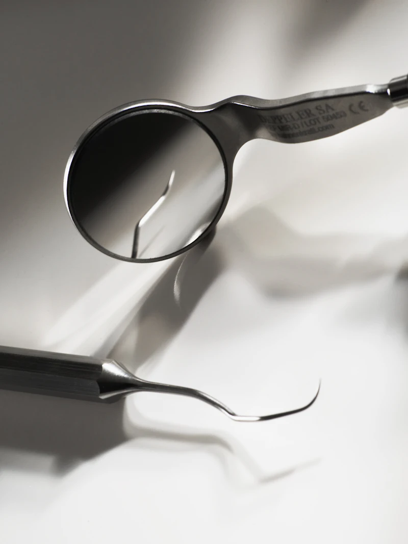 A dental mirror and a thin metal probe on a white surface