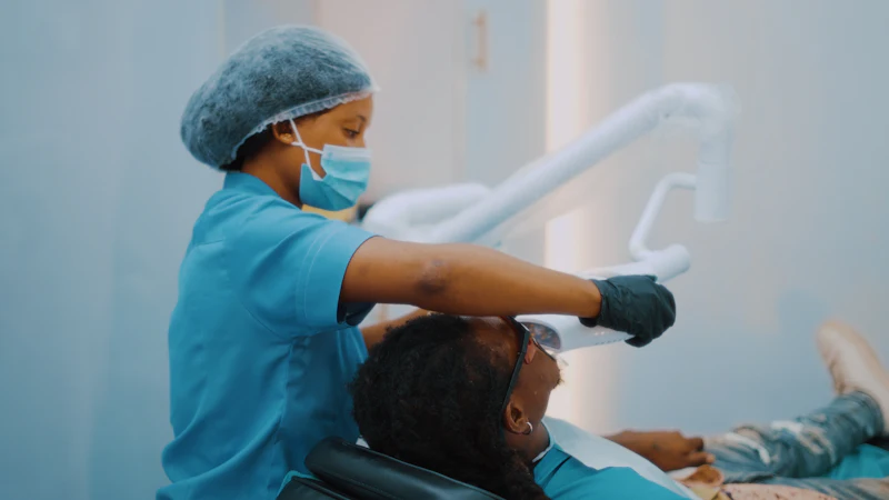 A dental assistant settles a patient in a dental chair under the treatment light